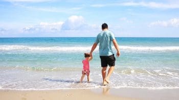 Pai segurando a m&atilde;o de sua filha na praia, caminhando juntos , simbolizando a conex&atilde;o e o amor no Dia dos Pais