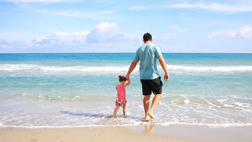 Pai segurando a mão de sua filha na praia, caminhando juntos , simbolizando a conexão e o amor no Dia dos Pais