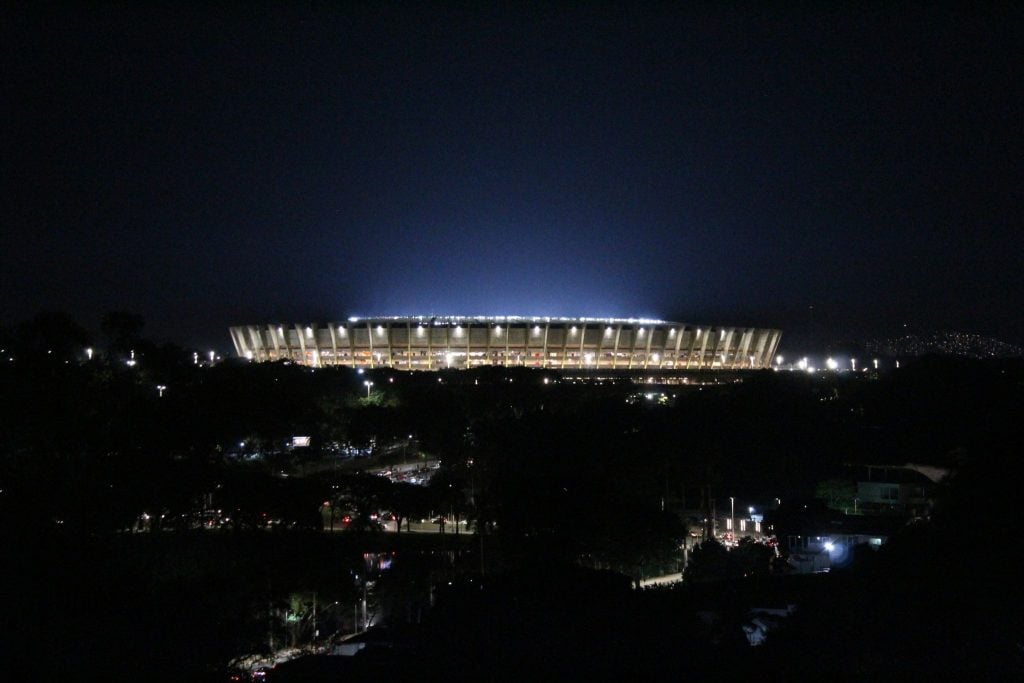 Vista panor&acirc;mica e noturna do Est&aacute;dio do Mineir&atilde;o totalmente iluminado sob o c&eacute;u escuro.